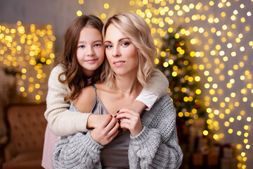 Christmas, love and family concept - portrait of mother and her daughter in decorated living room with Christmas tree and holiday lights