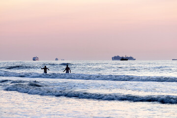 Naklejka premium Idle cruise ships parked near the Dutch beach where due to Covid pandemic at sunset; two person bathing in the water. 