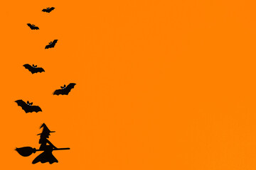 Silhouettes of a flock of bats and a witch flying on a broom made of black paper on an orange background. Halloween greeting template with copy space. Flat lay for your design. ready-made template