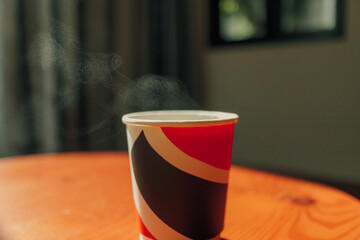 Hot drink in a paper cup on the table in warm morning light.