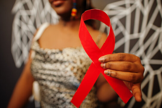 AIDS awareness. Stylish african american woman hold red ribbon against wall with wings.