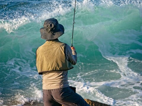 Pescador de espaldas echando el anzuelo contra las olas