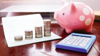 Selective focus on calculator with blur background stack of coins on book bank and pink piggy bank save , Financial discipline concept.