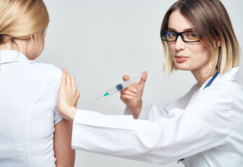 A woman doctor in a medical gown is giving an injection to a patient - obrazy, fototapety, plakaty