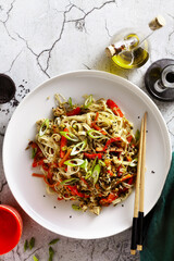 vegan pad thai rice pasta with vegetables and tofu on gray concrete background with soy sauce and sesame oil