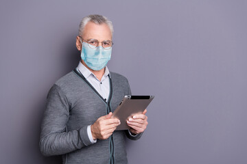 Portrait of old man wearing casual formal-wear mask holding in hands e-book isolated over gray pastel background