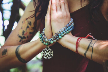Female hands doing namaste mudra yoga practice in forest with mala necklace - 386942513