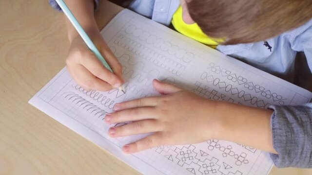 Video close up of boy writing different lines with pencil. Prewriting practice to prepare hands to write letters. Children education concept. View from above