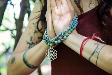 Female hands doing namaste mudra yoga practice in forest with mala necklace - 386942772