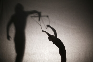 Shadow of woman silhouette holding a man like in a puppet show. Manipulation and dependence/control concept. Film edit. Selective focus. Copy space.