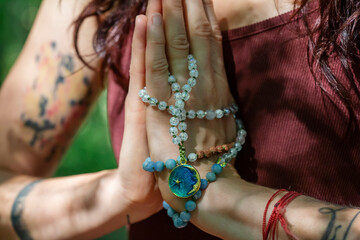 Female hands doing namaste mudra yoga practice in forest with mala necklace