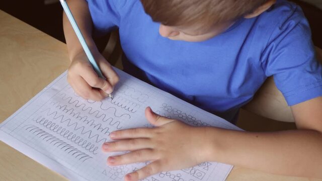 Video of cute boy writing different lines with pencil. Prewriting practice to prepare hands for write letters. Children education concept. View from above