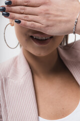 Beautiful laughing young woman covering her eyes with her hands over a light studio background