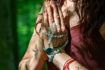 Female hands doing namaste mudra yoga practice in forest with mala necklace - 386944383