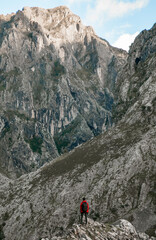 Fototapeta premium Man on the summit of a mountain with a red coat and a trekking backpack contemplating a large mountain in the background