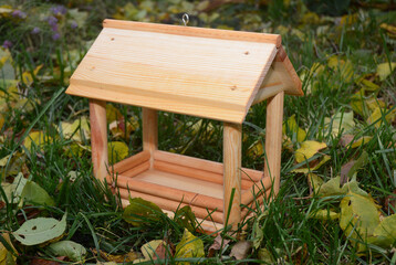 Fototapeta na wymiar A close-up on a wooden chalet style open sided wild bird platform feeder on the green grass with yellow fallen leaves around.