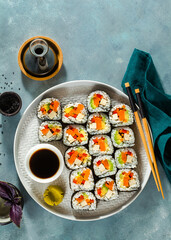 vegan sushi with tofu and vegetables on a blue table with soy sauce and black sesame seeds