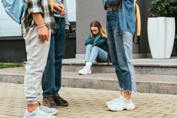 Selective focus of upset girl sitting near multiethnic teenagers outdoors