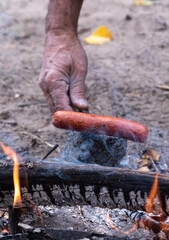 Obraz premium Hot Dog Roasting on Stick Over Open Flames of a Campfire with Hand Adjusting the Roasting Stick