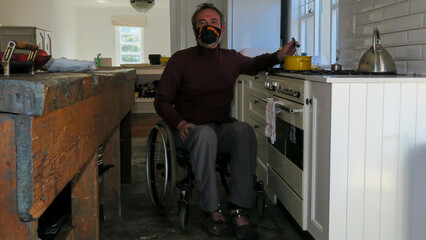 Male in a wheelchair cooking food in the kitchen. He is wearing a face mask in the th