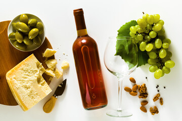 bottle of wine and glass on a white surface with parmesan cheese, olives, grapes and nuts. snack or wine advertisement