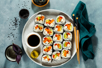 vegan sushi with tofu and vegetables on a blue table with soy sauce and black sesame seeds