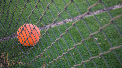 A basketball ball on the grass, a basketball field with a ball in it through the fences 