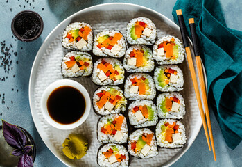 vegan sushi with tofu and vegetables on a blue table with soy sauce and black sesame seeds
