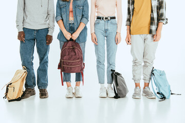 Cropped view of multiethnic teenagers with backpacks on grey background