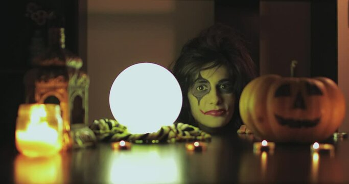 Female with scary halloween mask with pumpkin and crystal magic ball. 