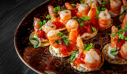 set of Appetizer canape with shrimp, cheese and sauce on a small loaf of bread in plate on black wooden table