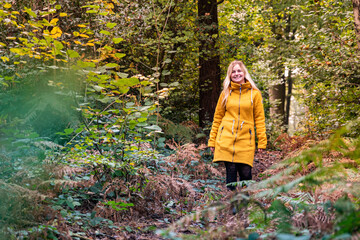Blonde woman in yellow jacket walking along a forest path 	