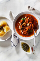 Ukrainian soup borsch with mushrooms and white beans and pampushki buns on a marble table