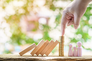 Man pokes gold coin with his finger for protect family from hazards from falling wooden blocks in the public park, Saving money or loan for buy insurance of real estate protection concept.