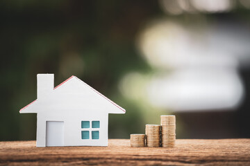 Stack gold coin with growing and wooden home model put on the blue vintage wood board on bokeh in the public park, Saving money for buy house and loan to business investment for real estate concept.
