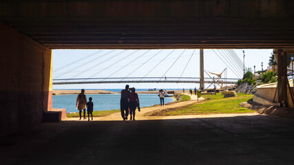 Varias personas paseando por el Parque fluvial de Fuengirola hacia el puente de la Armada.