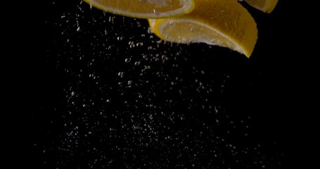 fresh orange fruit slices splashing into water on black background. slow motion - Powered by Adobe