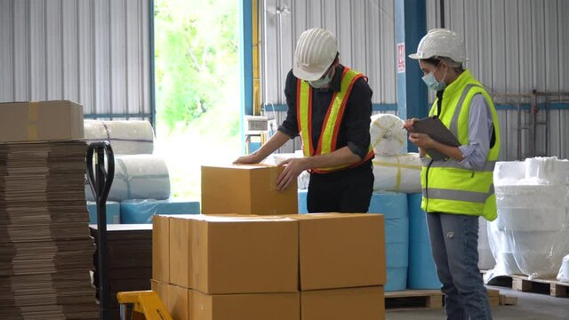 warehouse worker wearing medical face mask lifting box  moving to pallet. manager woman checking order with digital tablet for preparing goods for dispatch in distribution warehouse . loading parcel