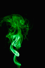 Whimsical curls and shapes of green smoke on a dark background. Streaming smoke from a burning incense stick.