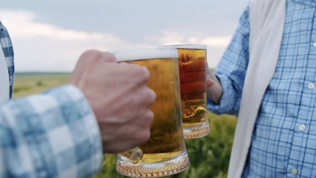 Close view of two men drinking a pints of dark and light beer in barley field