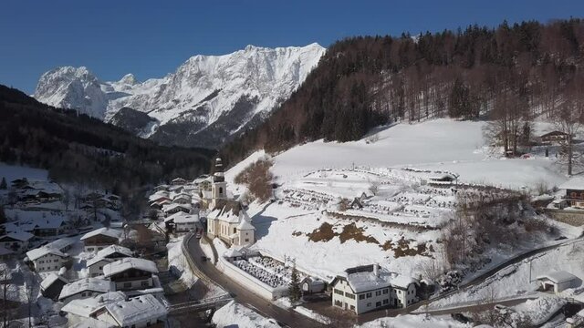 Winter flight over Ramsau town and famous Parish church St. Sebastian, Berchtesgaden, Bavarian Alps, Germany