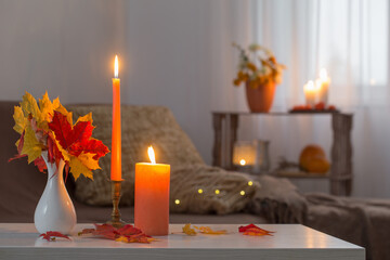 burning candles with autumn decor on white table at home