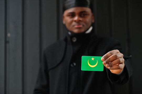 African man wear black durag hold Mauritania flag at hand isolated dark background.