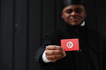 African man wear black durag hold Tunisia flag at hand isolated dark background.