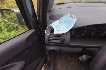 Face mask at the front of a car while driving. Covid 19 safety measures while traveling. 
Hygienic mask are placed on the black console on the inside of the car, where the sunlight comes in.