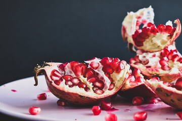 Juicy pomegranate on a pink plate and black background.
