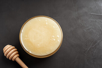 White lime honey in a transparent bowl on a dark table near the Mace for honey and copying space