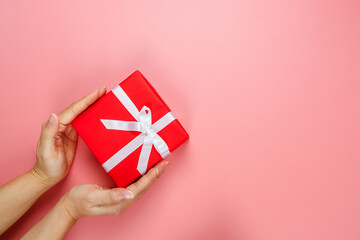 Flat lay of woman hands holding gift wrapped and decorated with bow isolated on pink background.