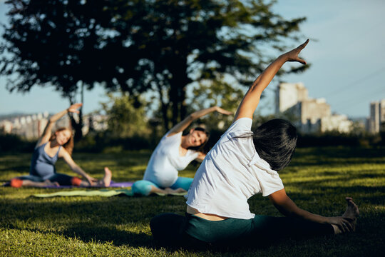 Yoga Instructor Showing To The Pregnant Women Exercises While Sitting On The Yoga Mat Outside.