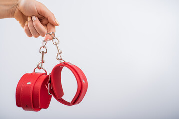 Red leather handcuffs in female hands on a white background. BDSM accessories